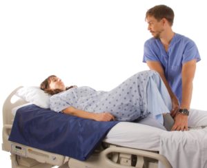 A patient is lying on their back in bed with knees bend up on top of one slide sheet folded in half while the caregiver is helping them boost up in bed.